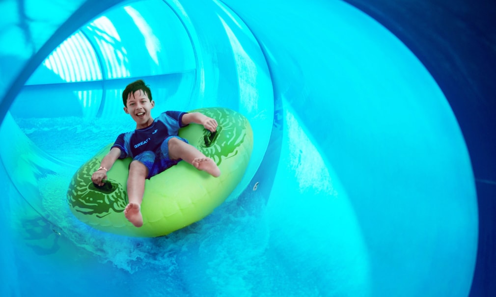 Boy rides down blue waterslide on yellow tube 