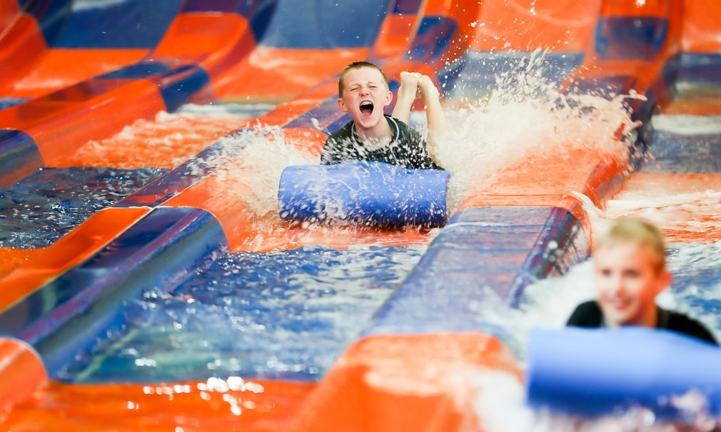 Two kids race down a waterslide laying on a blue mat