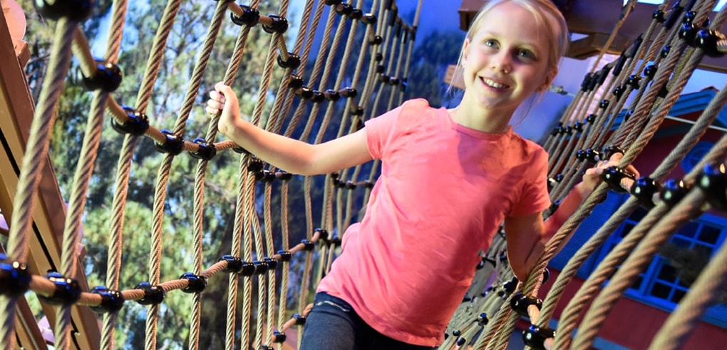 Young girl with a pink shirt navigating indoor ropes course
