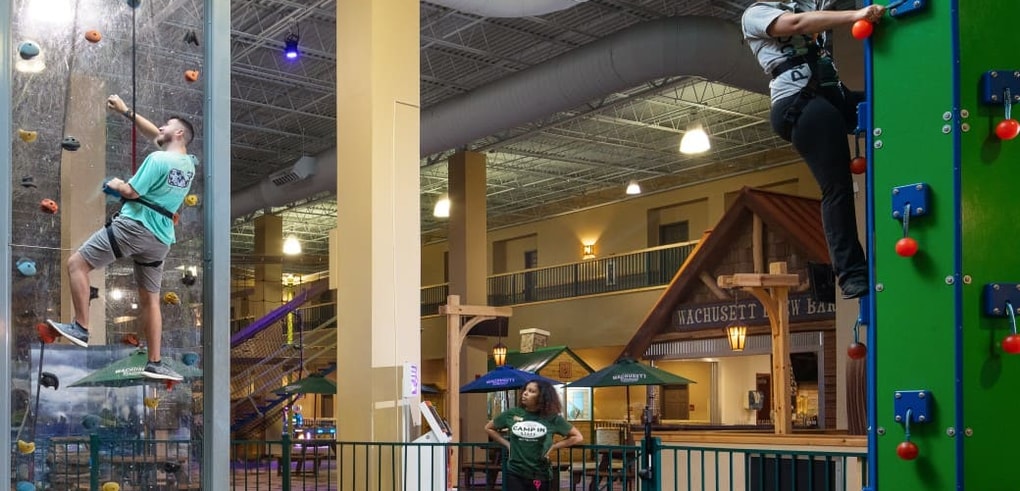 Family climbing an indoor rock wall with safety harnesses