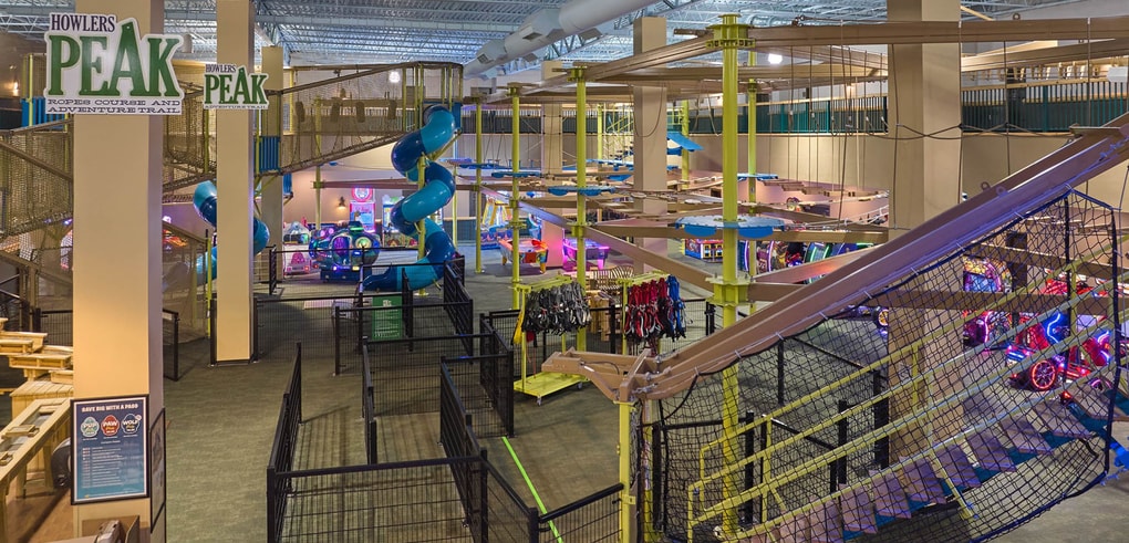 Three women navigating indoor ropes course with harnesses