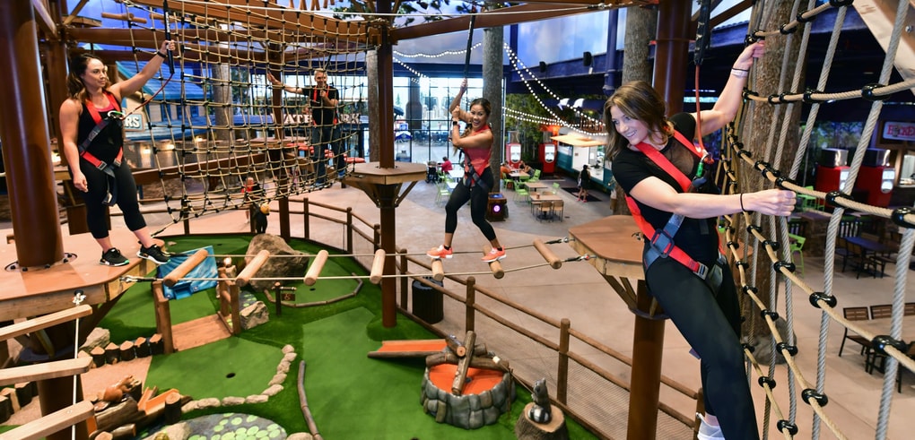 Three women navigating indoor ropes course with harnesses