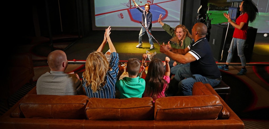 Family cheers as child plays an interactive hockey game on a large screen