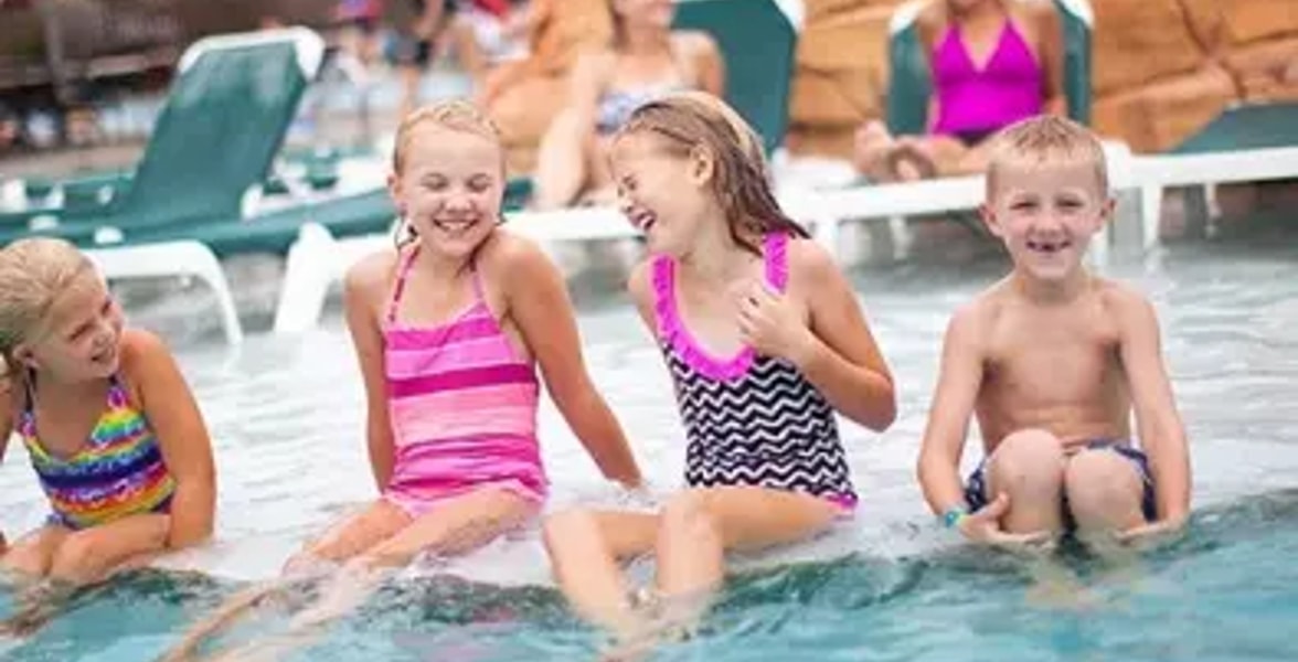 Four kids smile and laugh as they sit in a shallow outdoor pool 