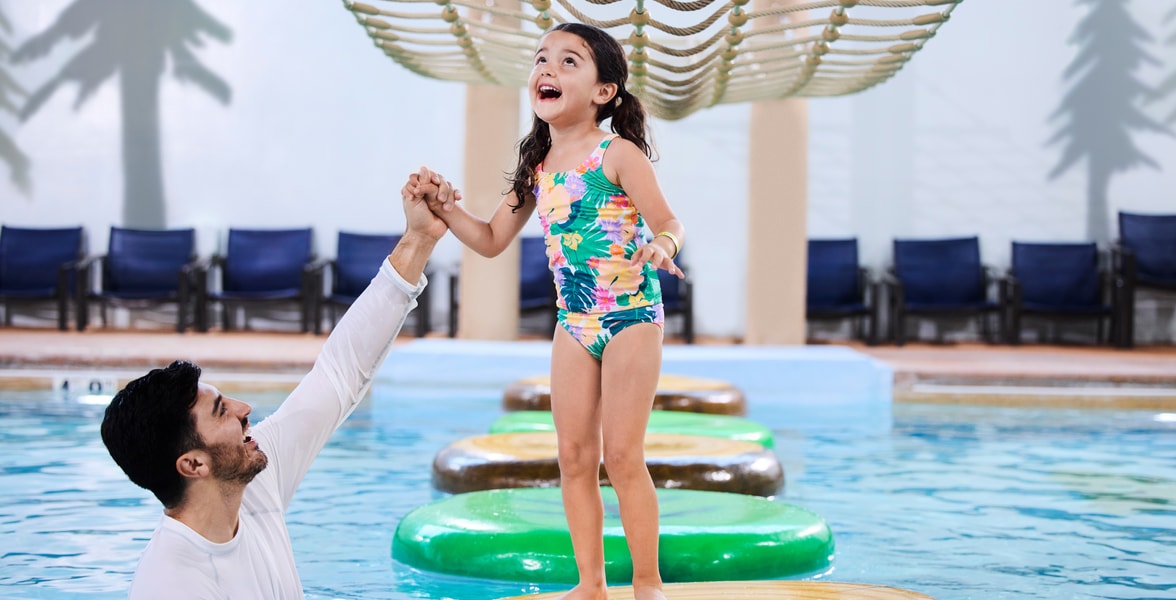 A girl balances on a lily pad float in indoor pool