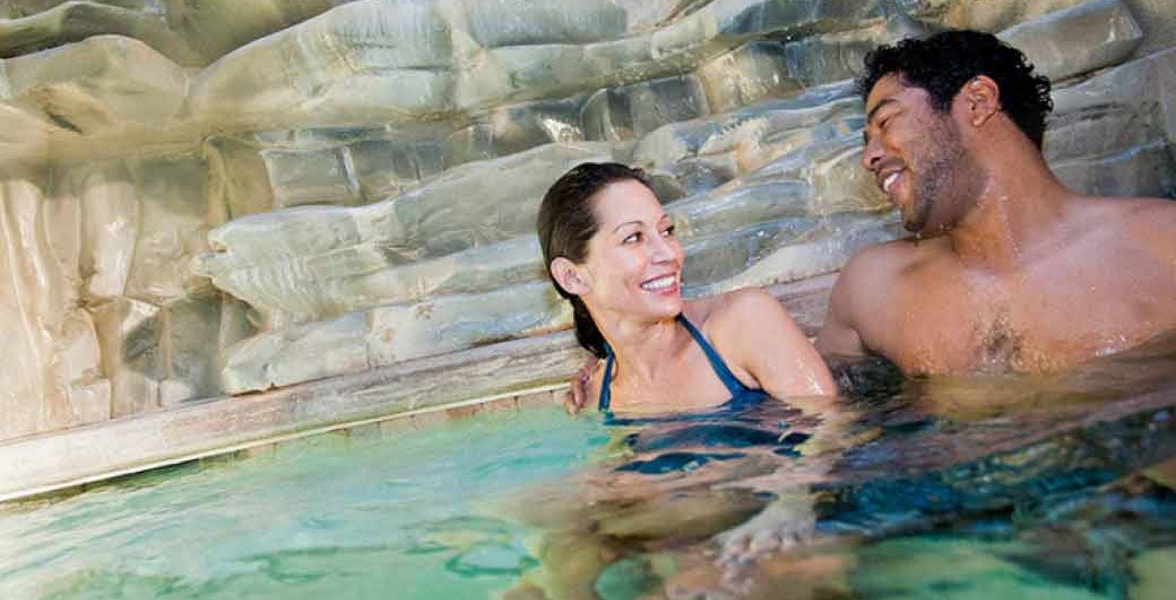 A couple relax in and on the side of the indoor pool 