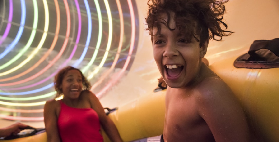 Two kids in yellow raft going fast down a colorful waterslide