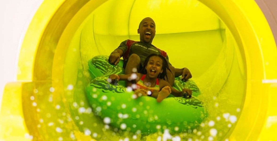 Dad and daughter ride down yellow waterslide in green tube