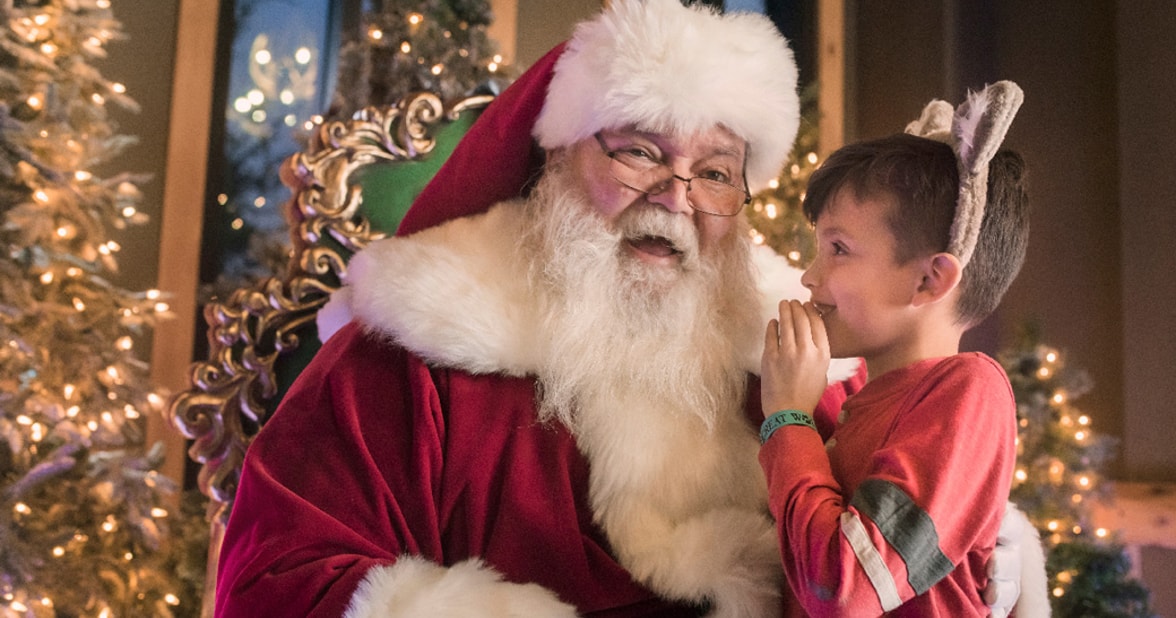 Boy wearing wolf ears and whispering to Santa's ear