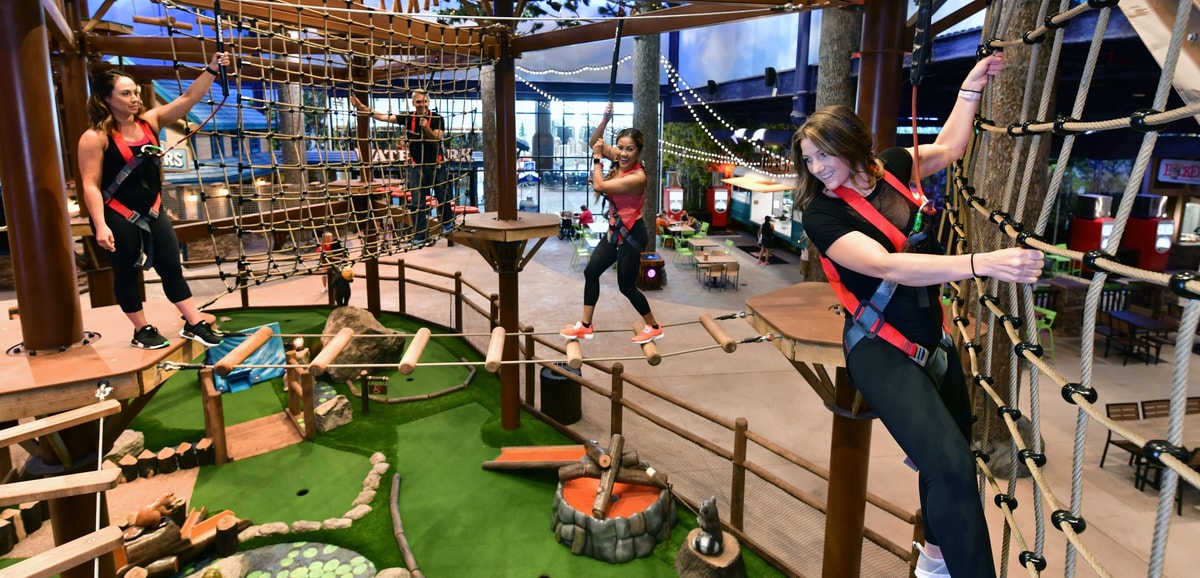 Three women navigating indoor ropes course with harnesses