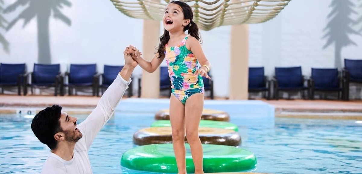 A girl balances on a lily pad float in indoor pool