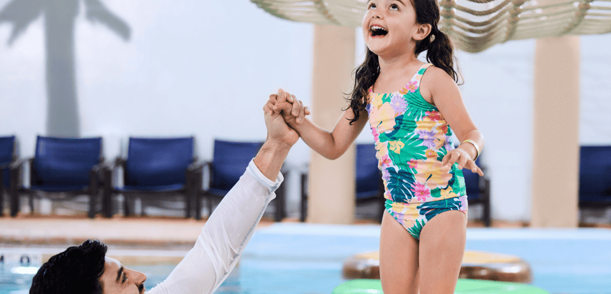 A girl balances on a lily pad float in indoor pool