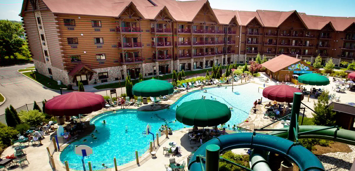 Aerial view of outdoor pool area featuring water slides, shaded seating under colorful umbrellas, and guests enjoying a sunny day.