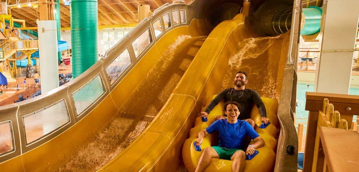 Boy rides down blue waterslide on yellow tube 