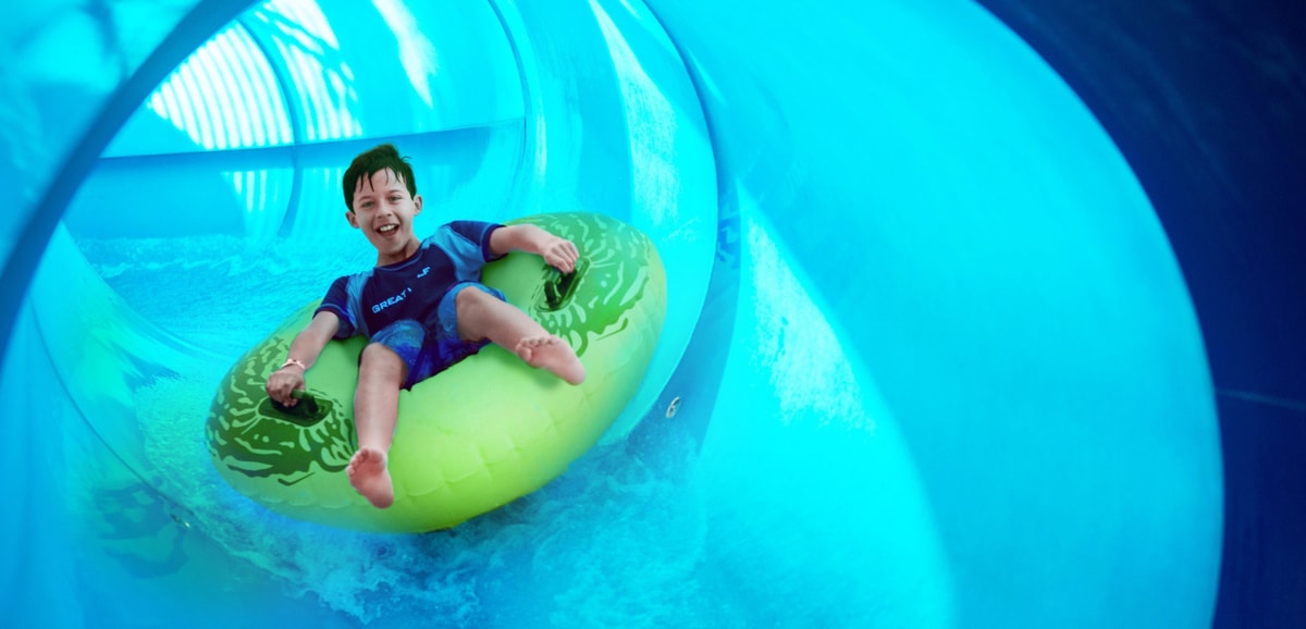 Boy rides down blue waterslide on yellow tube 