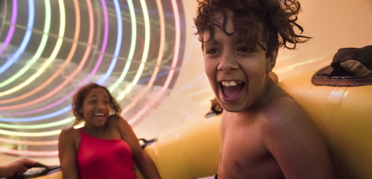 Two kids in yellow raft going fast down a colorful waterslide
