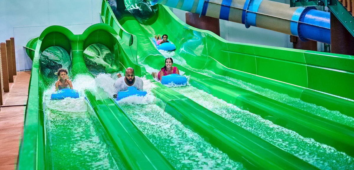 Guests race down a waterslide laying on a blue mat