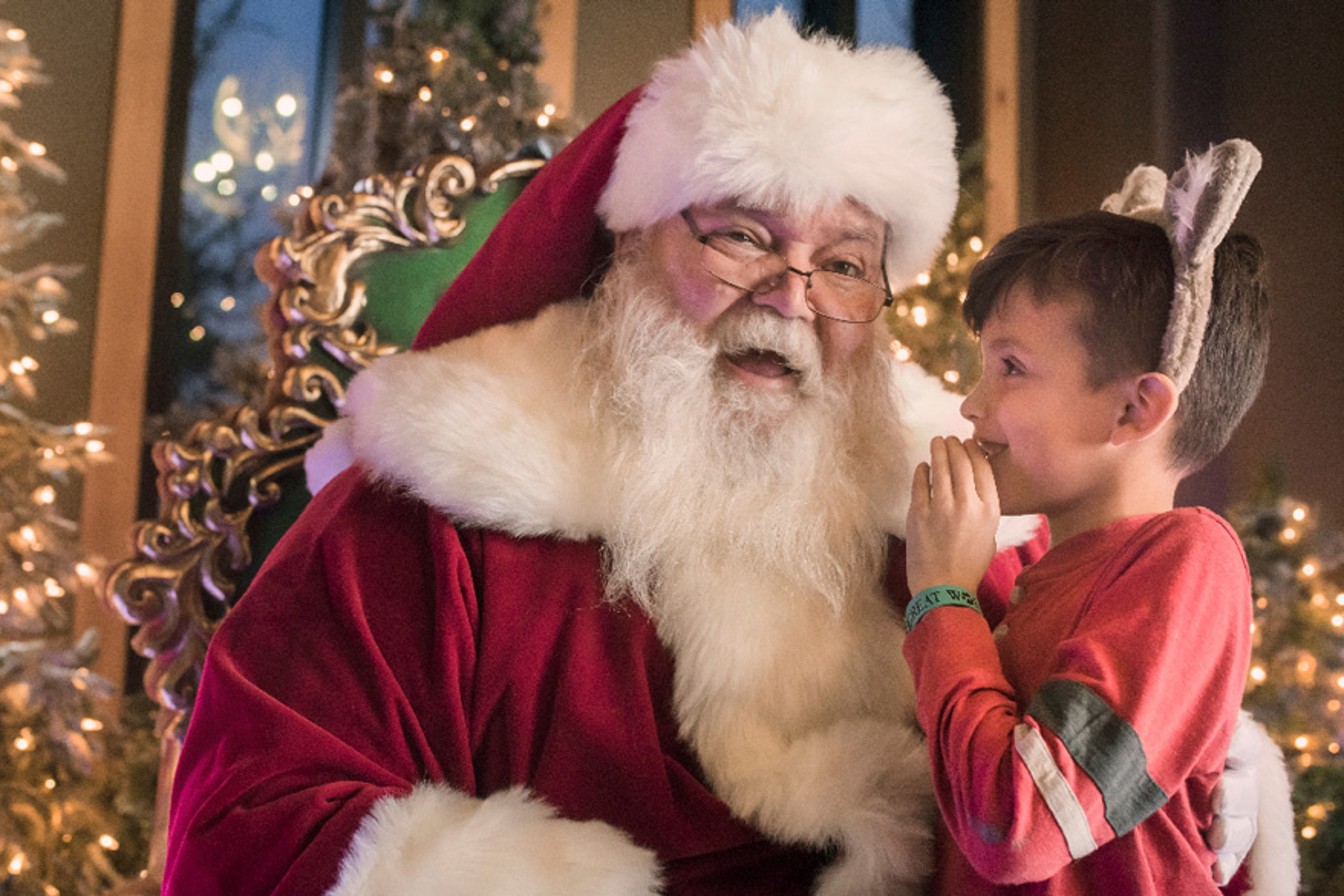 Boy wearing wolf ears and whispering to Santa's ear