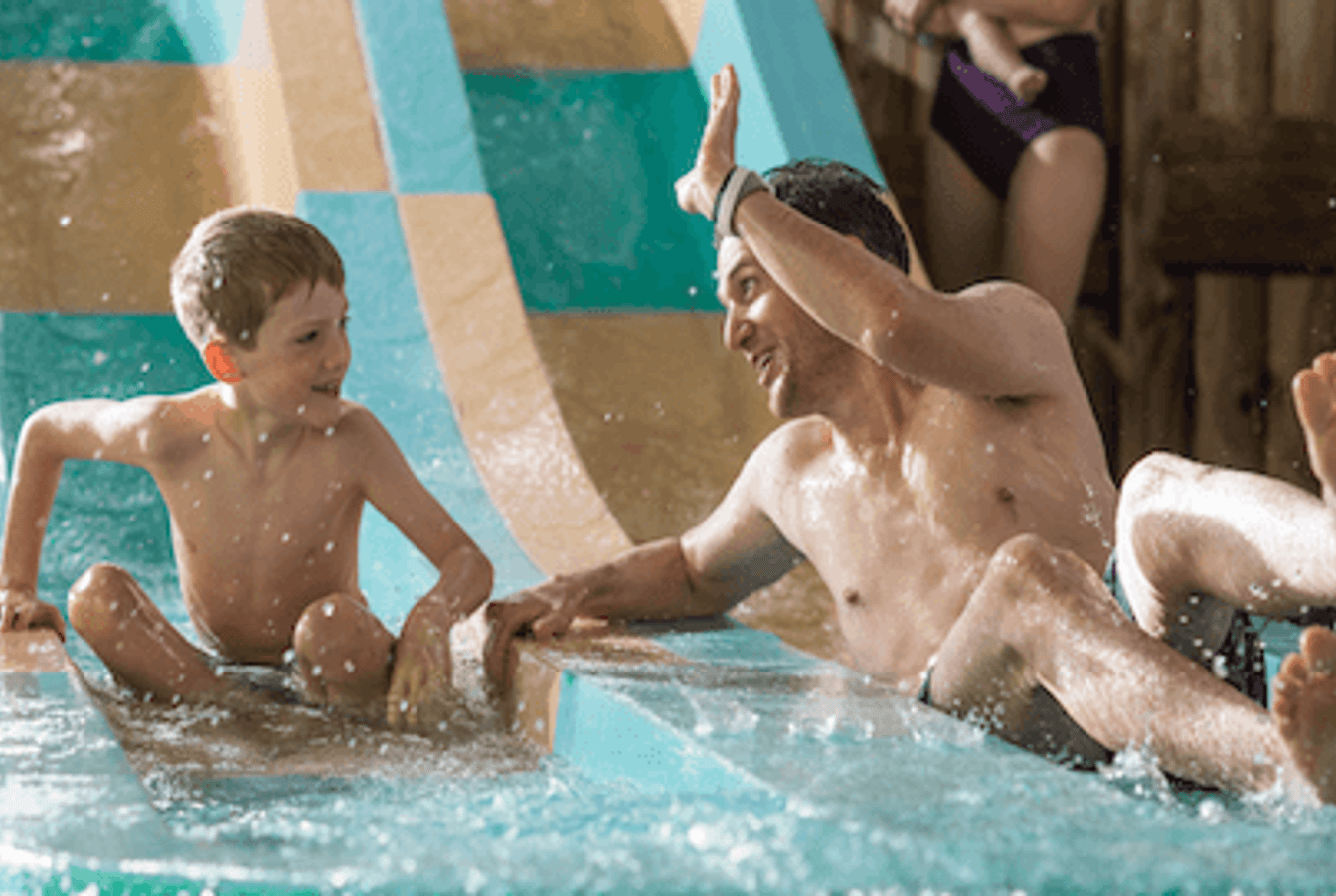 A father and son smile together while going down a slide 