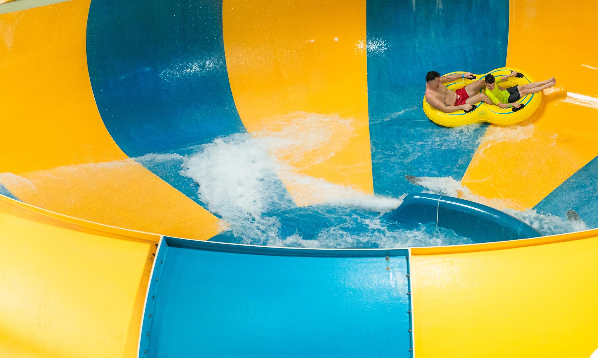 A father and son going down the Coyote Cannon water slide together on a yellow raft.