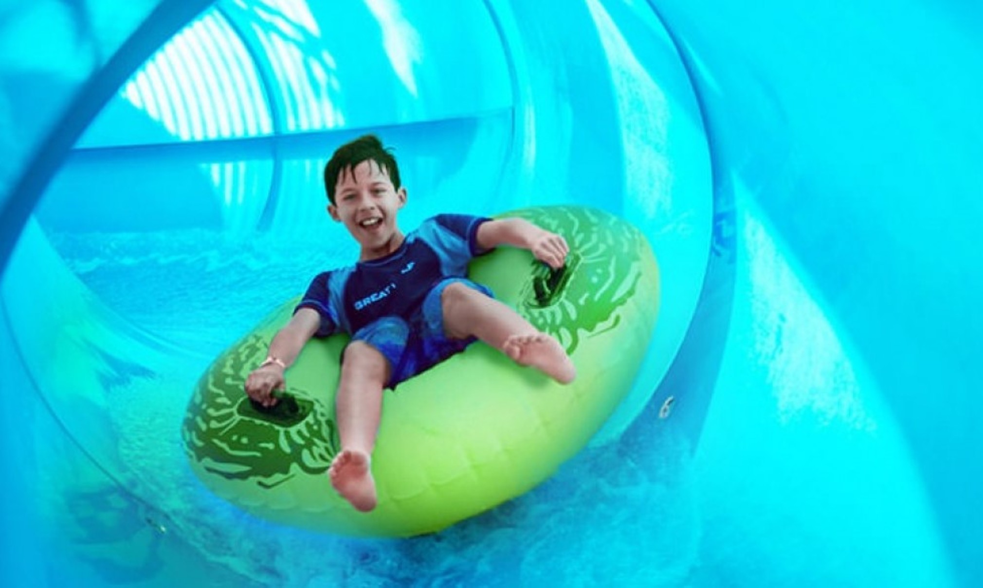 Boy rides down blue waterslide on green tube 