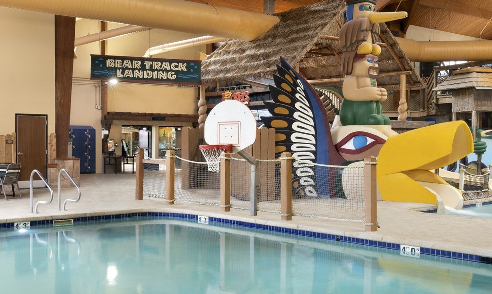 Indoor pool featuring a water slide and a basketball hoop for recreational activities.