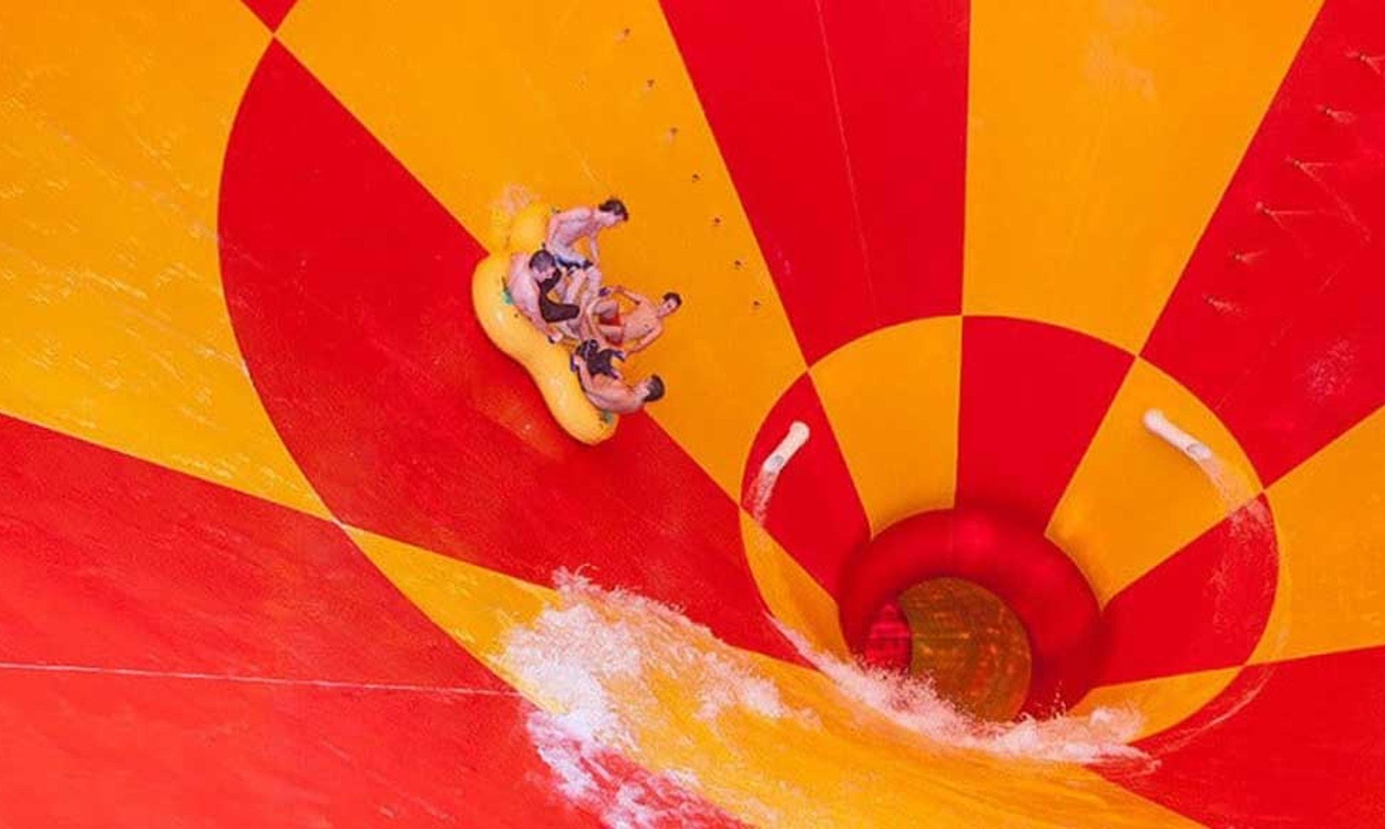 Four friends ride down a multicolored water slide in a tube 
