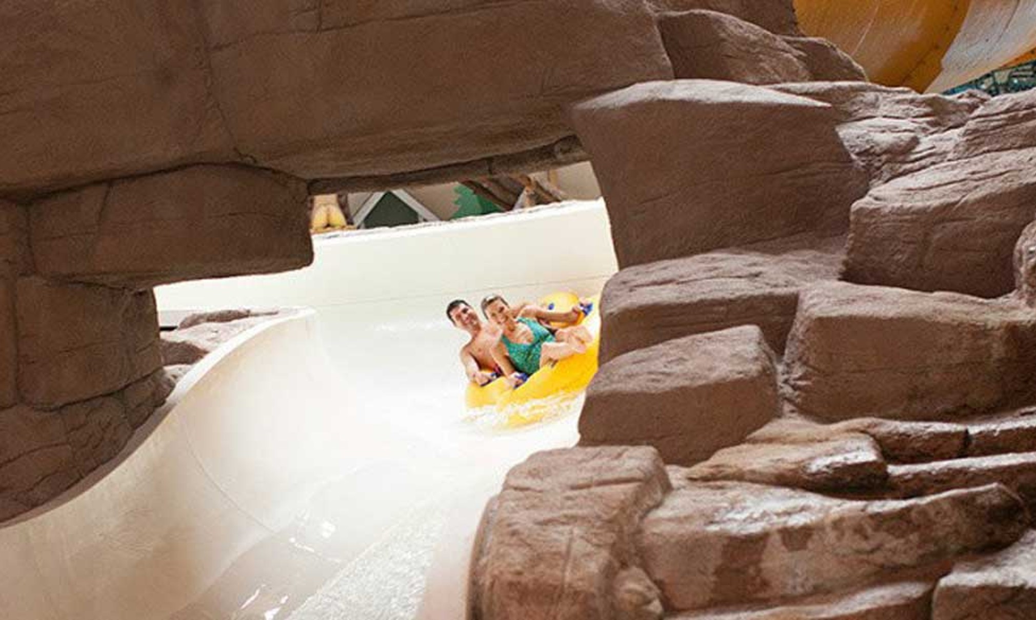 A couple in a tube race down the water slide surrounded by rock decor