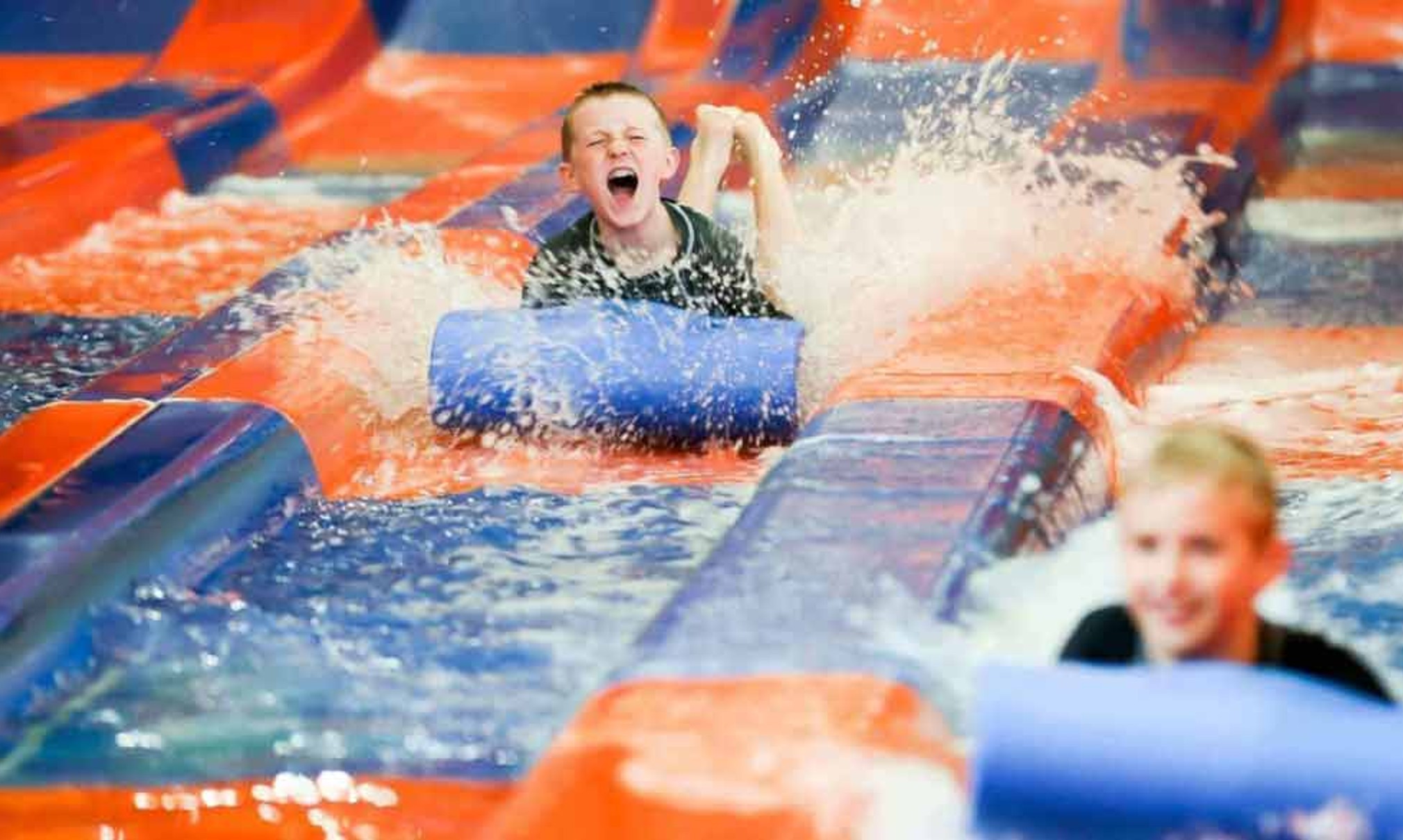 Two kids race down a waterslide laying on their stomaches 