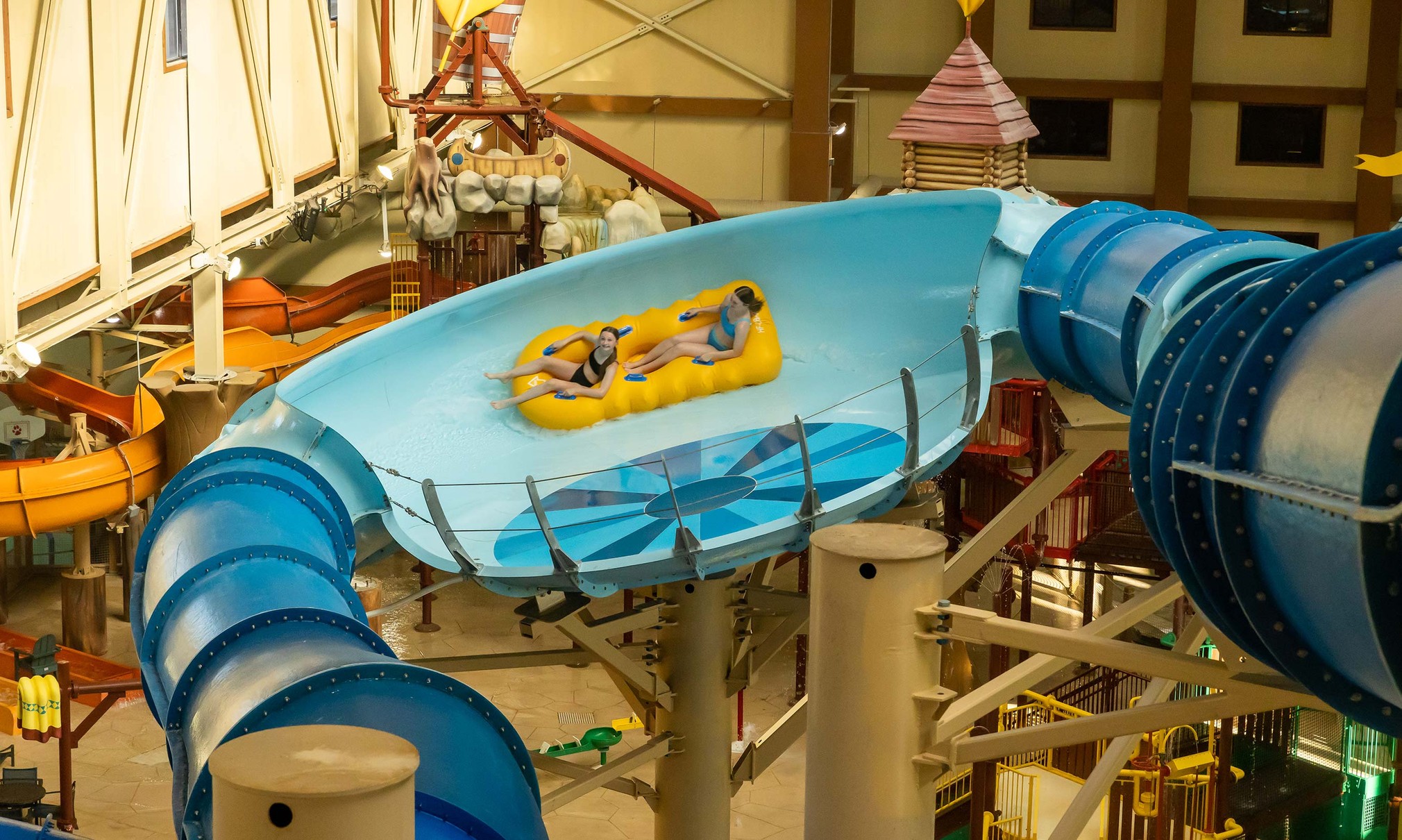 Two teenagers riding a yellow raft in an indoor water park