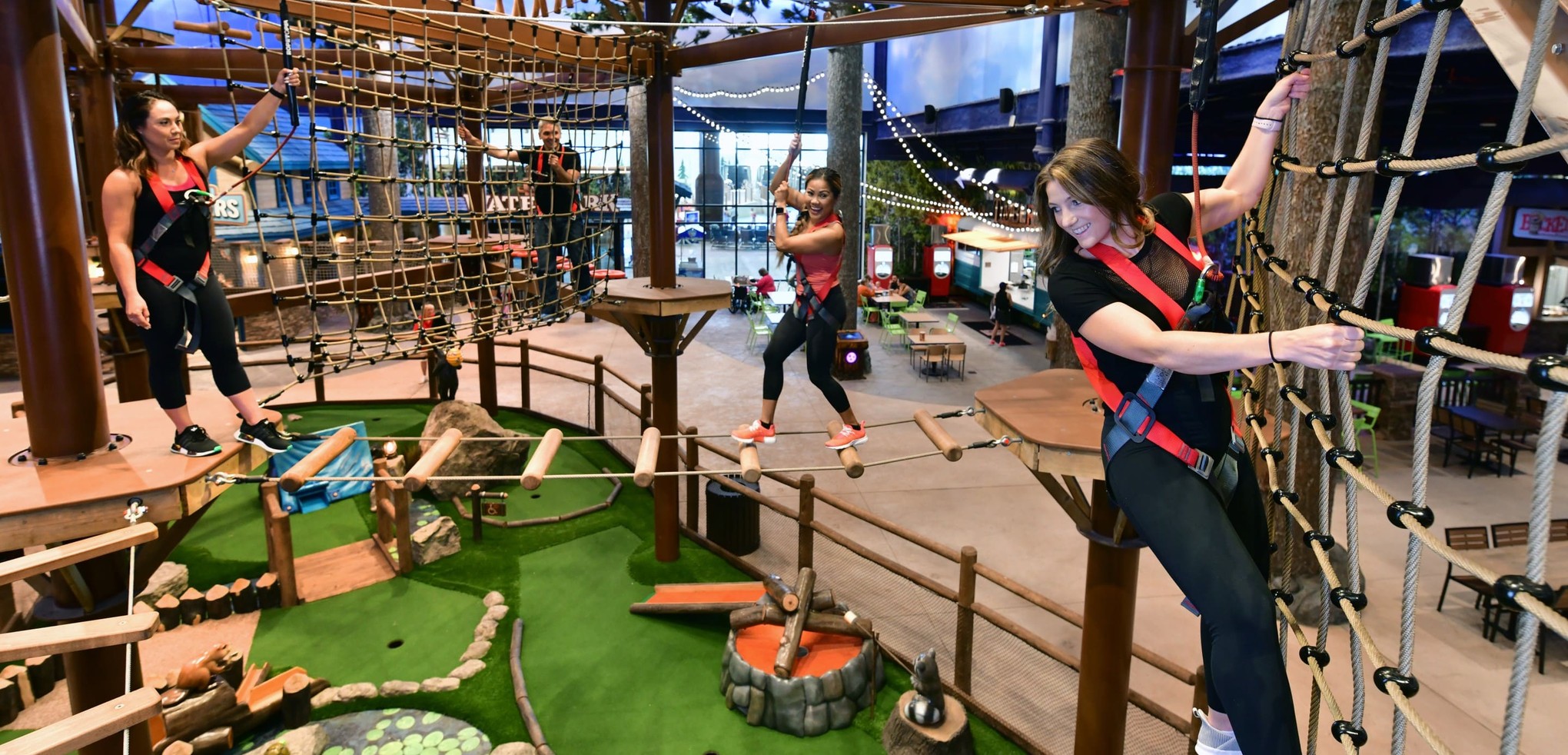 Three women navigating indoor ropes course with harnesses