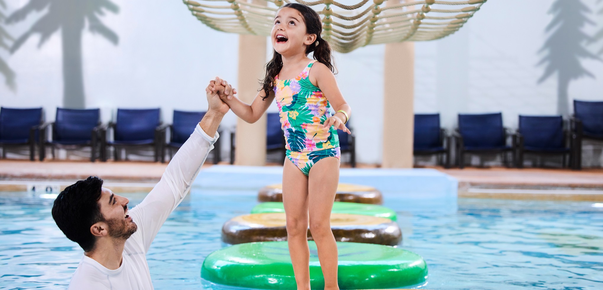 A girl balances on a lily pad float in indoor pool