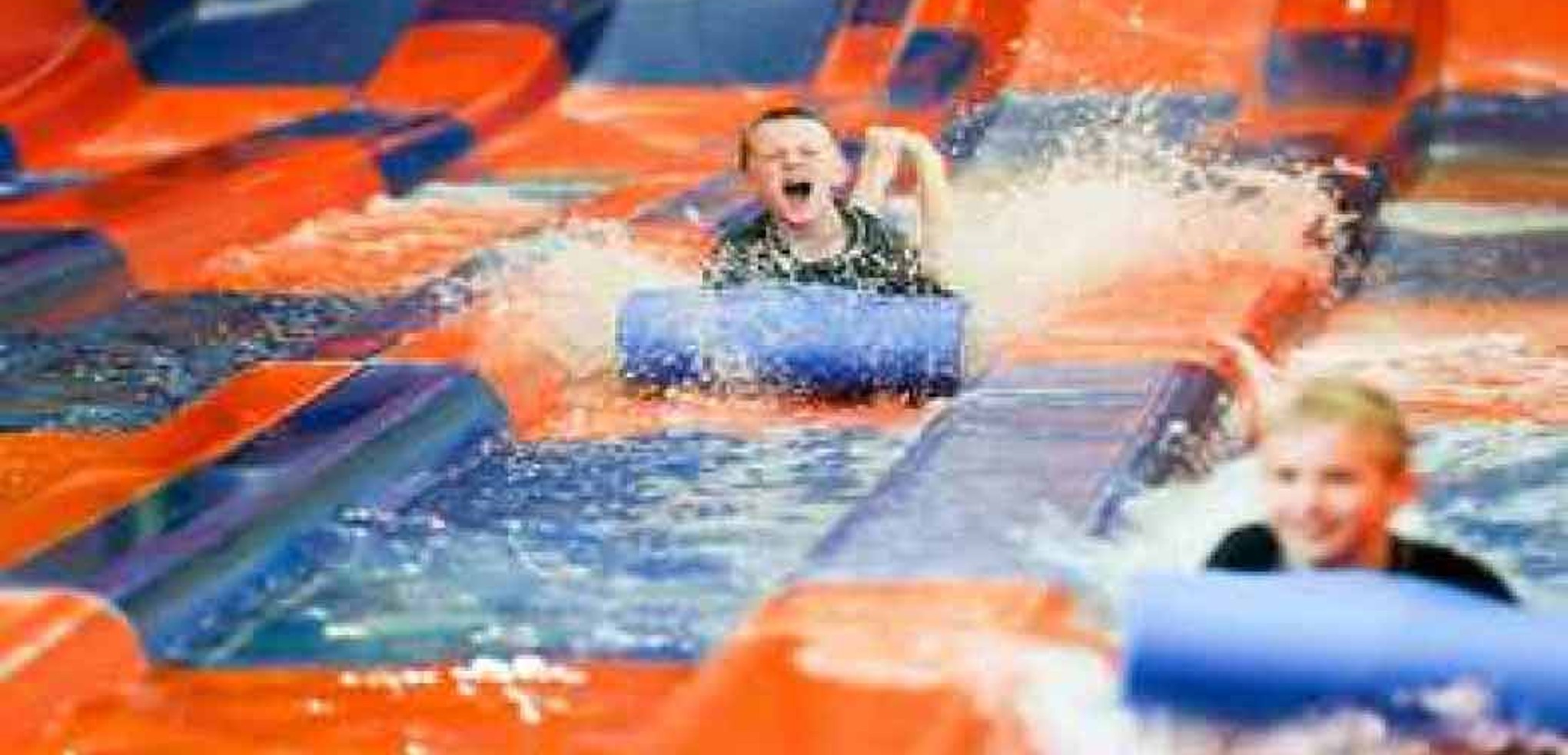 Two kids race down a waterslide laying on their stomaches 