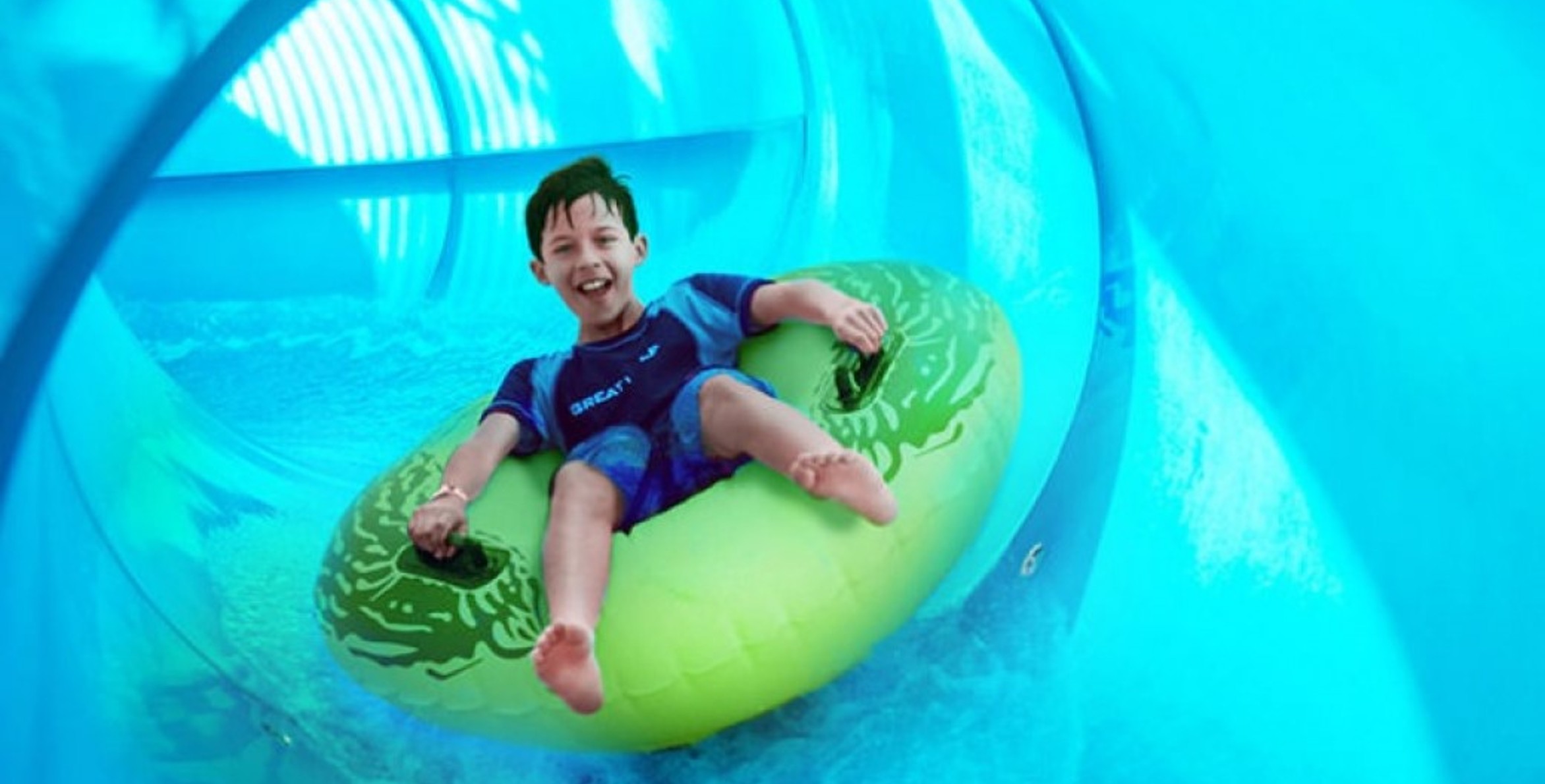 Boy rides down blue waterslide on green tube 