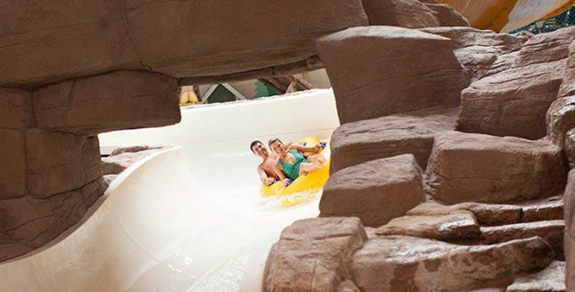 A couple in a tube race down the water slide surrounded by rock decor