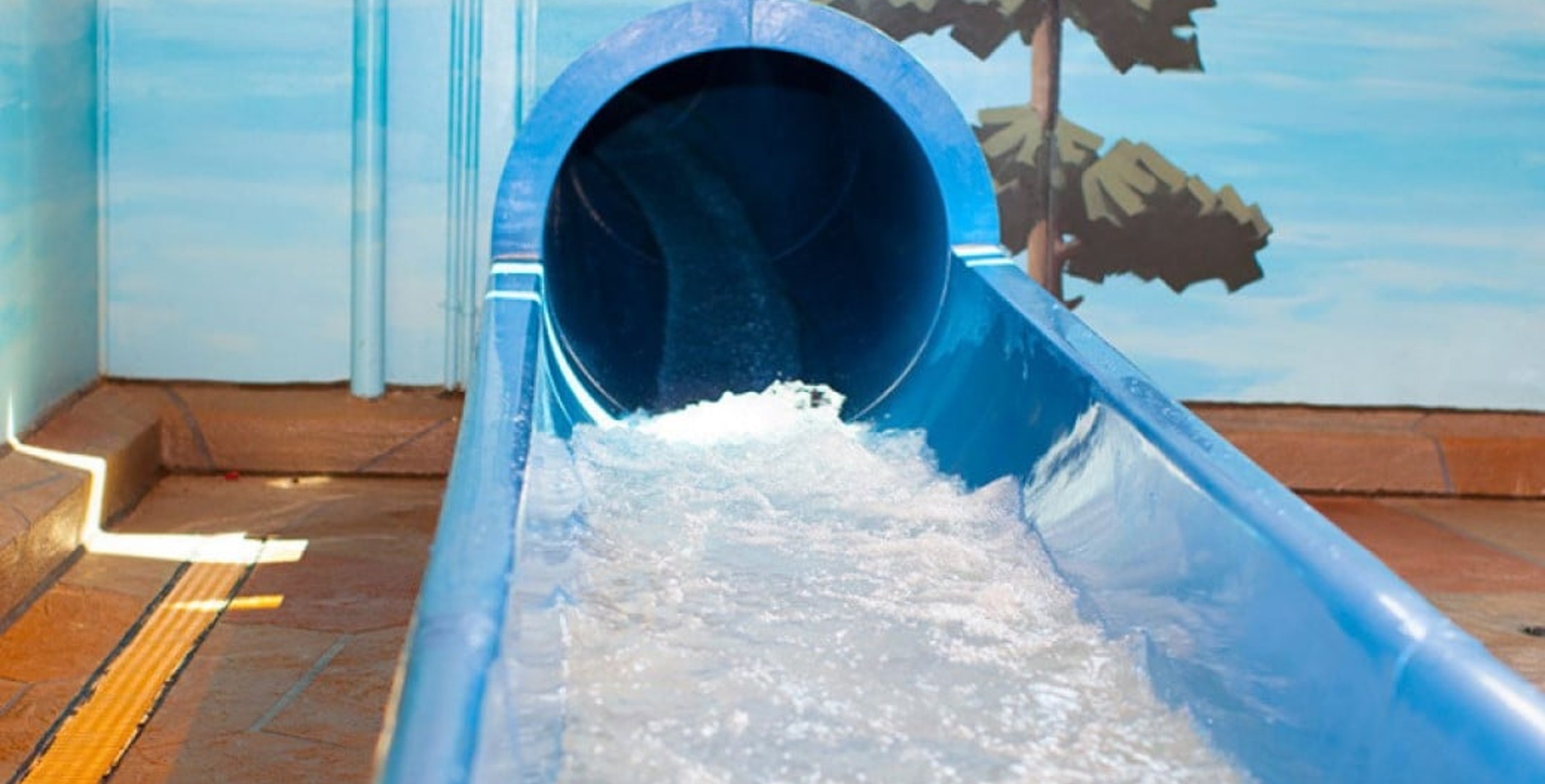 The end of a blue waterslide with water splashing out