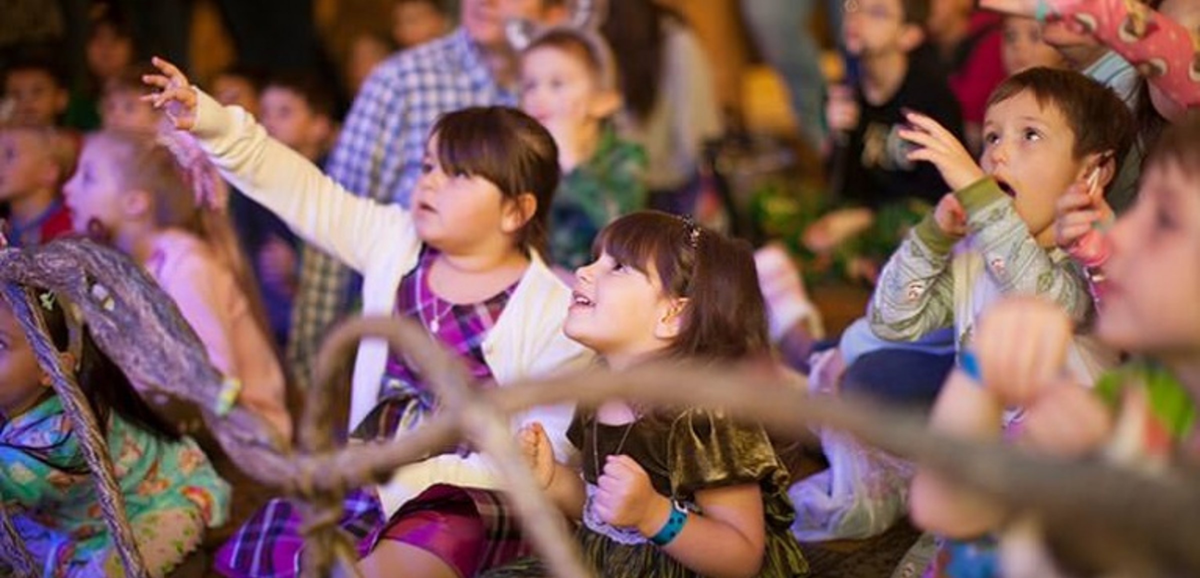 Kids raise their arms as they enjoy The Northwoods Friends Show in the lobby of a Great Wolf Lodge indoor water park and resorts.