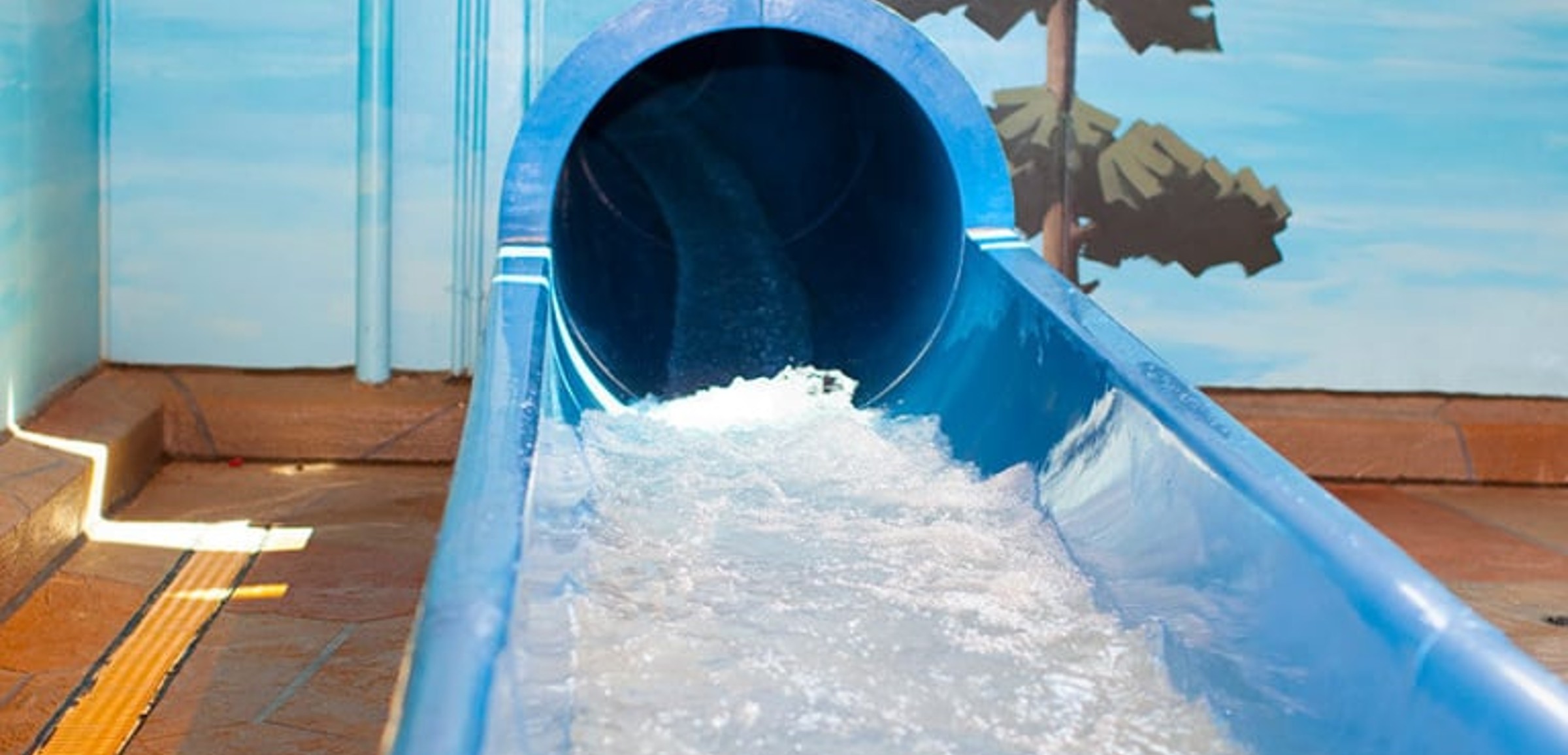 The end of a blue waterslide with water splashing out
