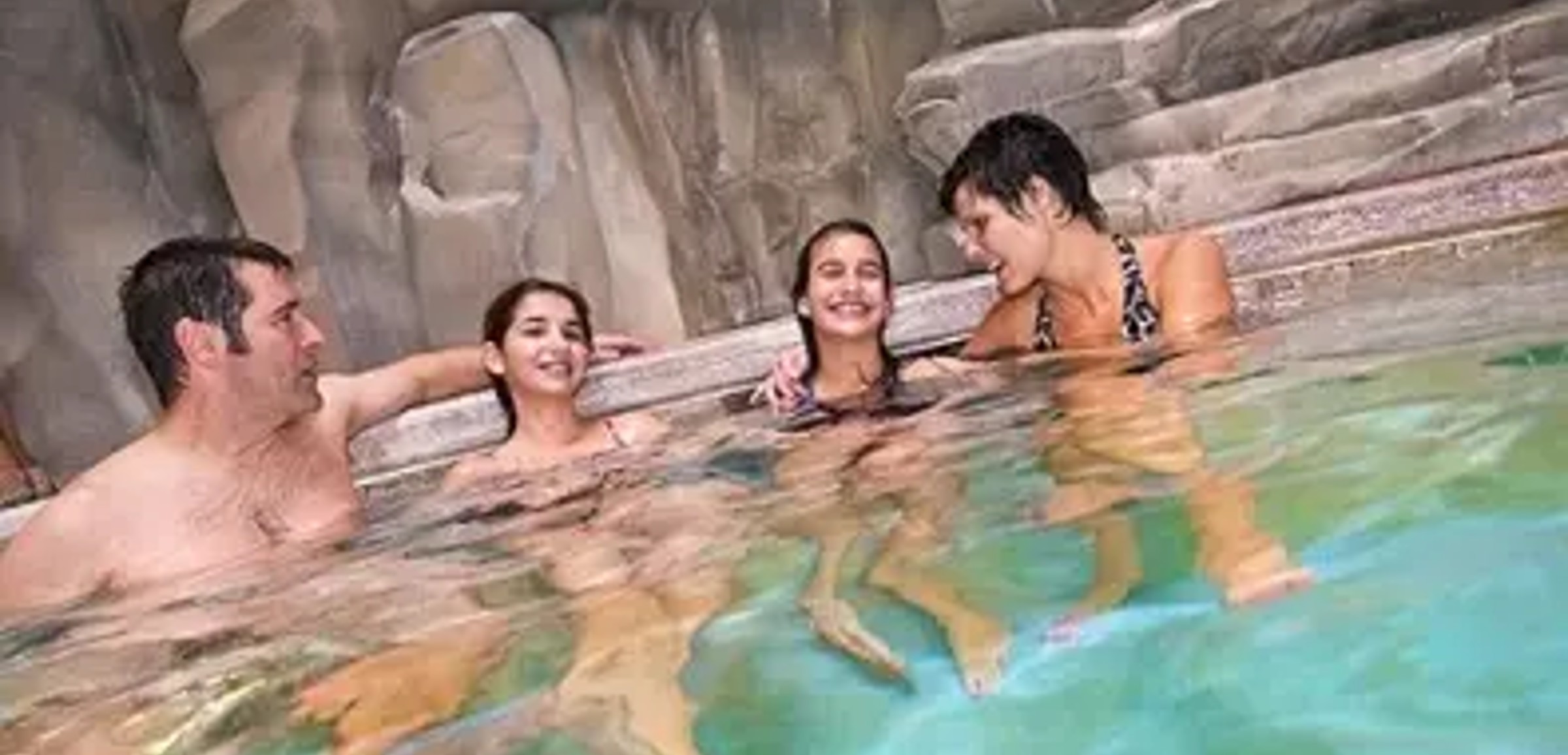 A family of four relaxes by the South Hot Springs pool at Great Wolf Lodge indoor water park and resort.
