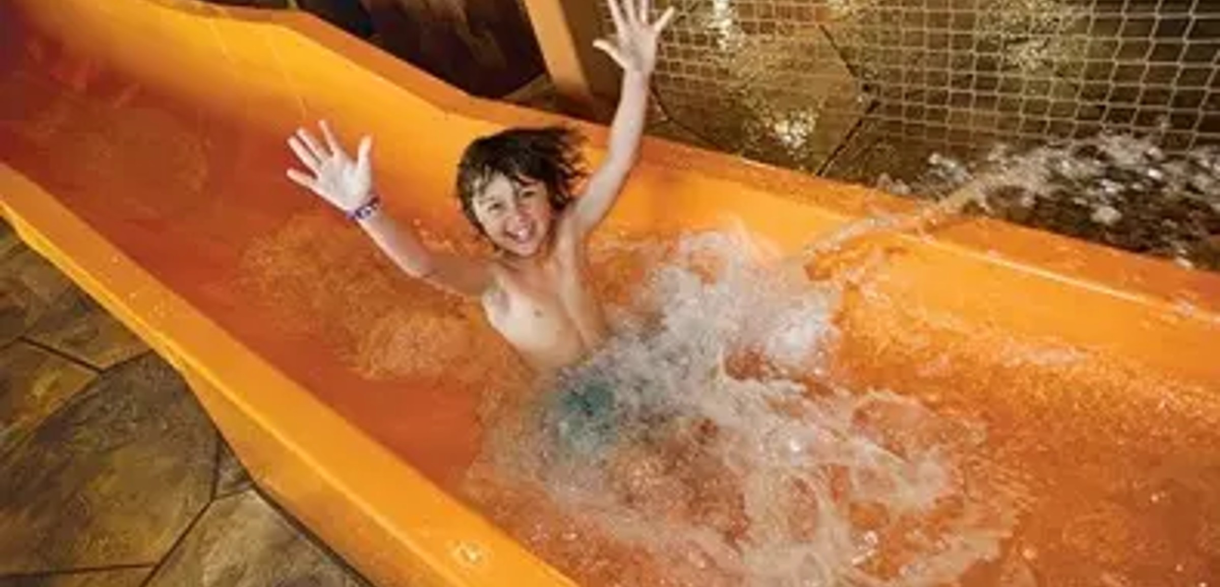 kid rides down waterslide with hands up in the air