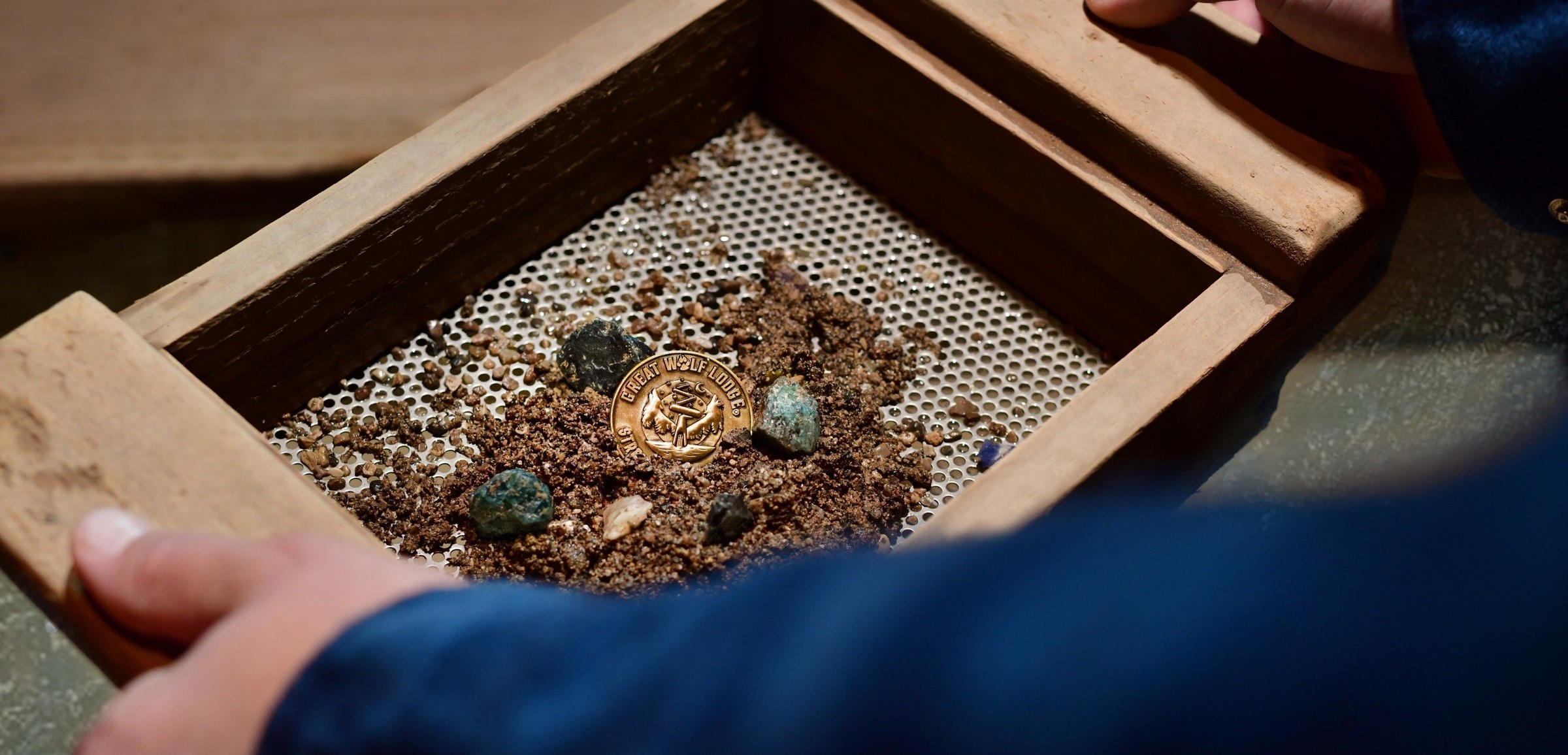 Hands holding sifter with gold coin, gems