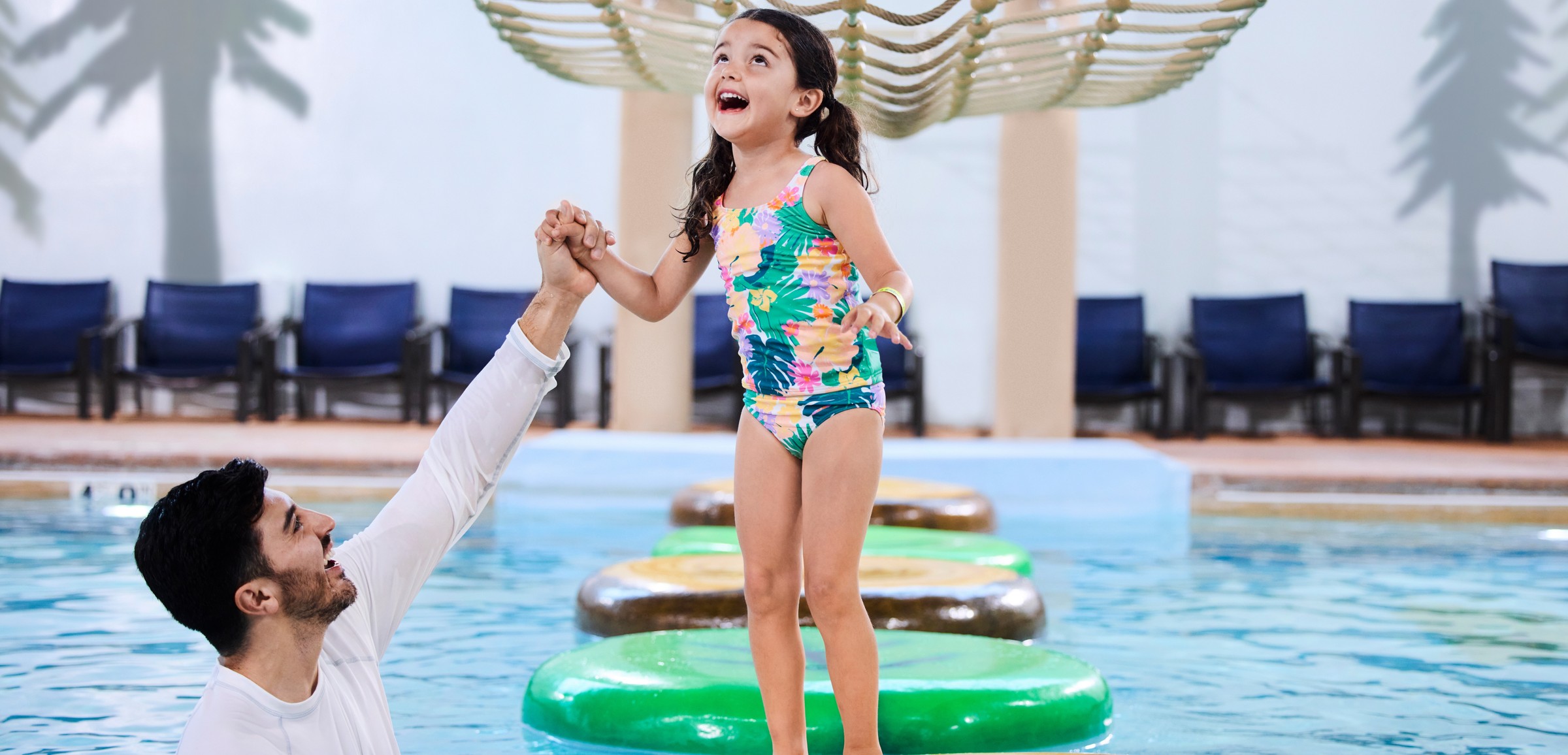 A girl balances on a lily pad float in indoor pool