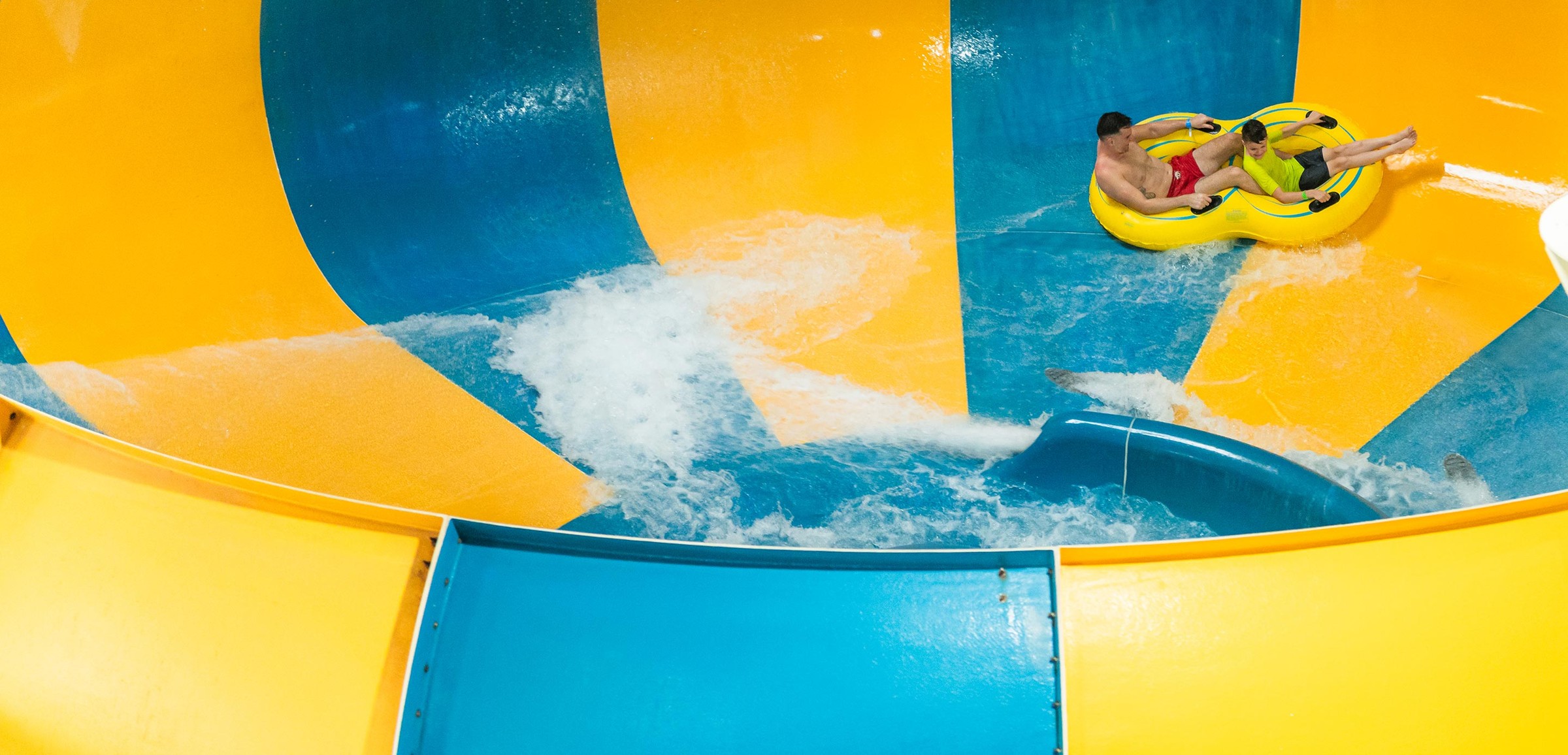 A father and son going down the Coyote Cannon water slide together on a yellow raft.