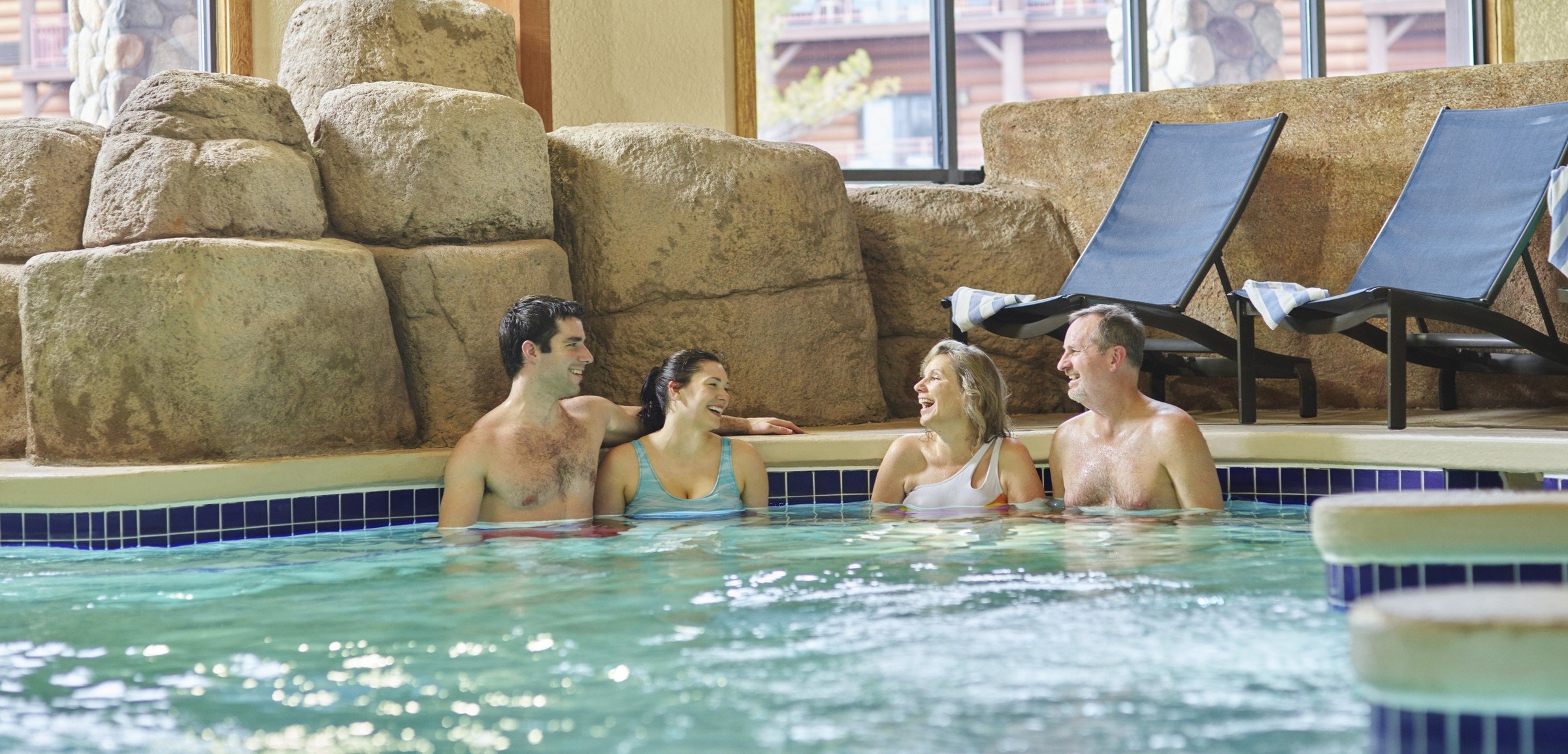 Two couples relax in an indoor hot tub