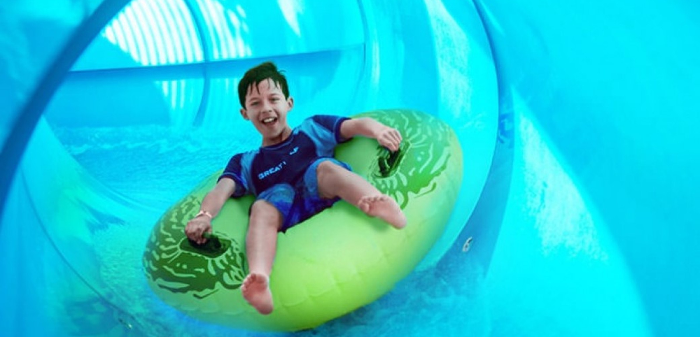 Boy rides down blue waterslide on green tube 