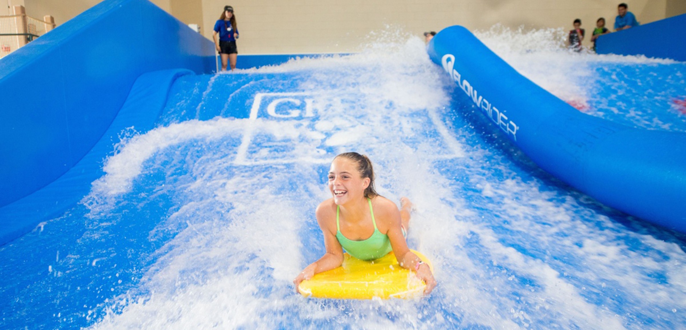 A child rides on a yellow boogie board in the water attraction 