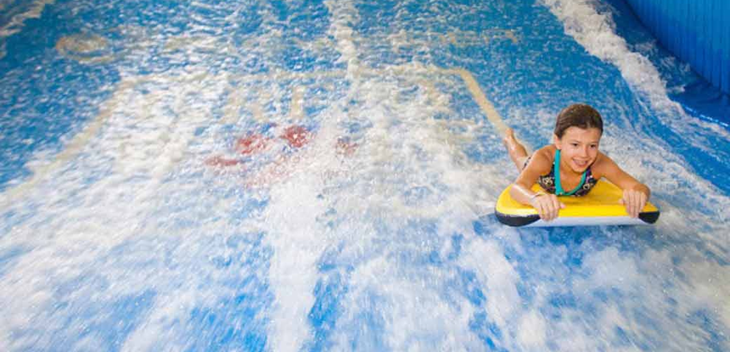 A child rides on a yellow boogie board in the water attraction 