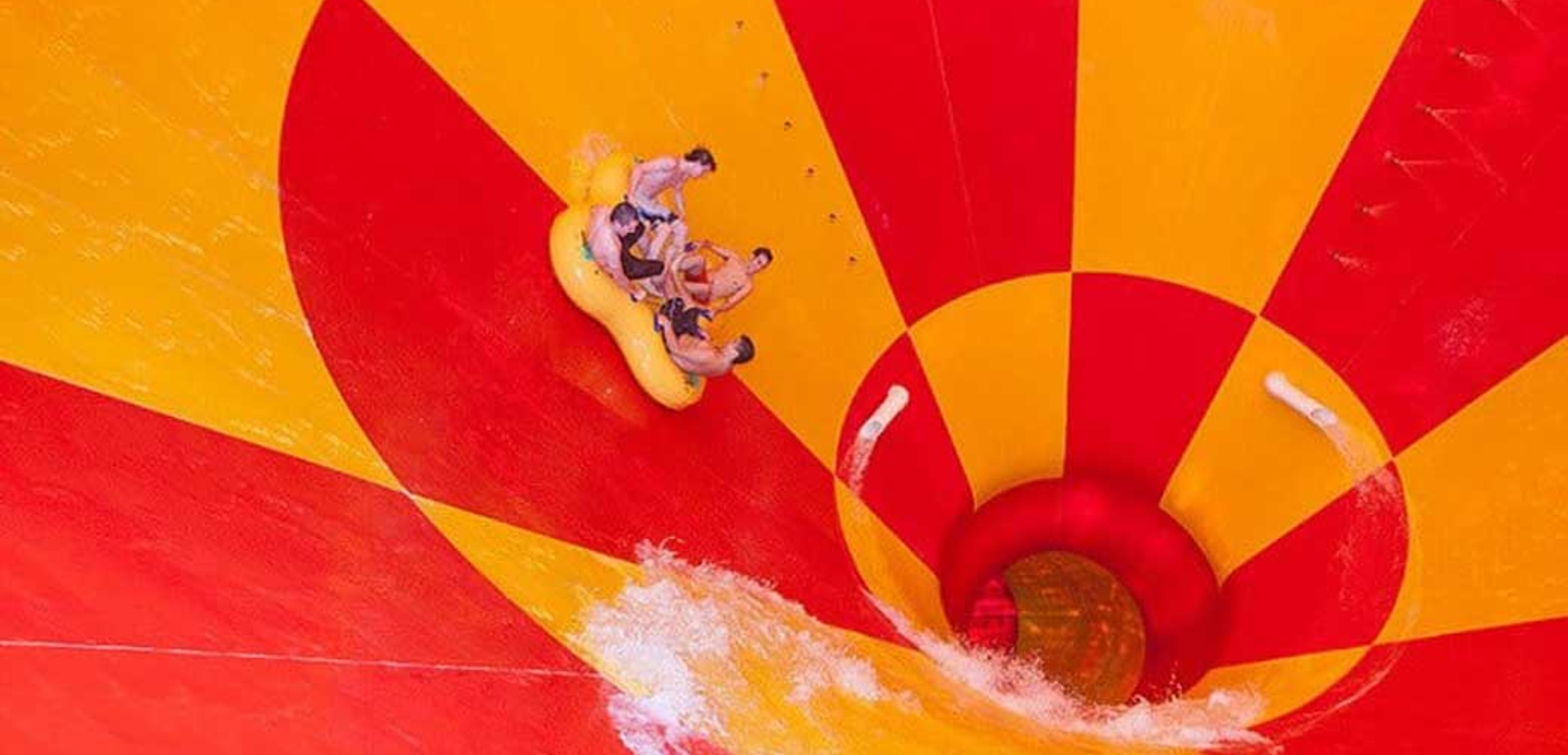 Four friends ride down a multicolored water slide in a tube 