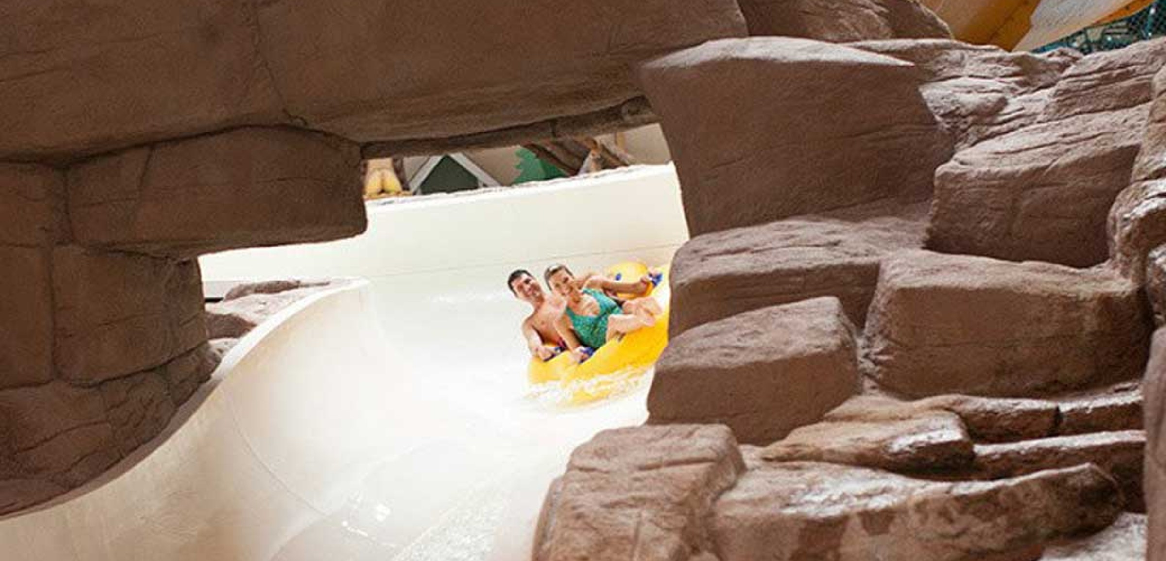 A couple in a tube race down the water slide surrounded by rock decor