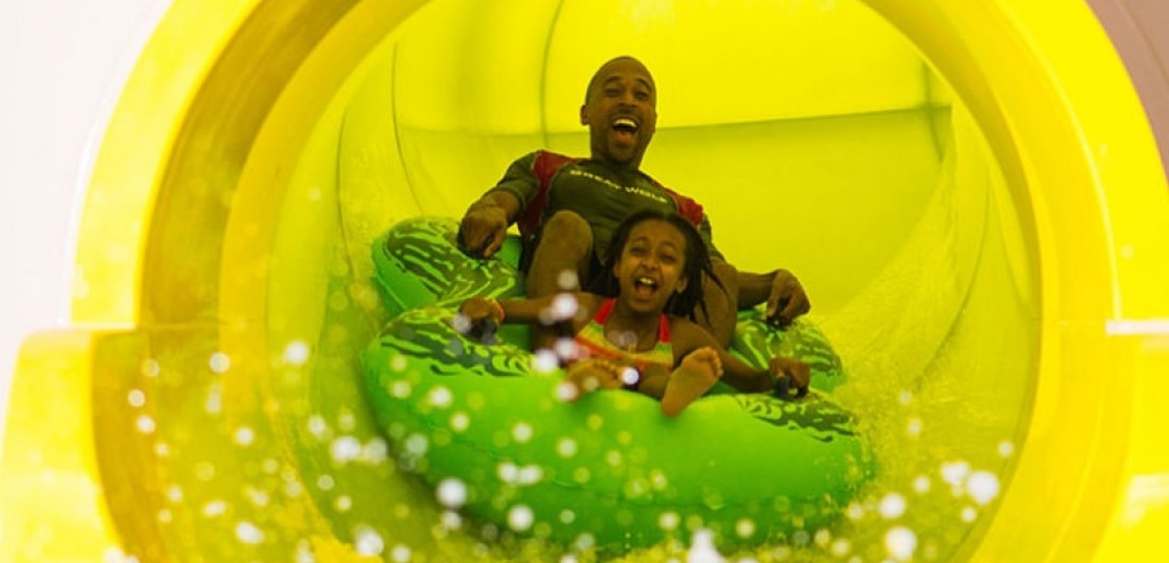 Dad and daughter ride down yellow waterslide in green tube